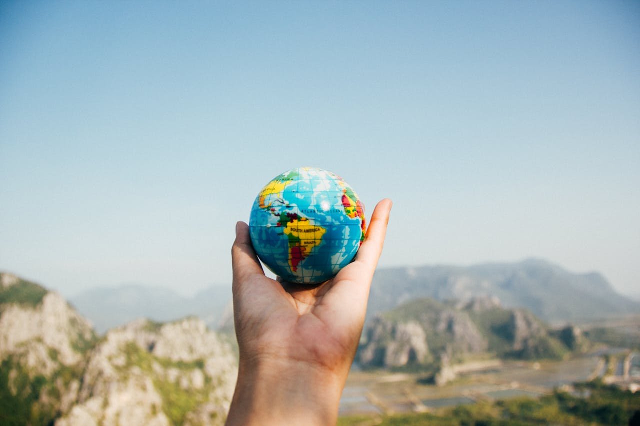 who-we-are Hand holding a globe against a mountain background symbolizing travel and exploration.